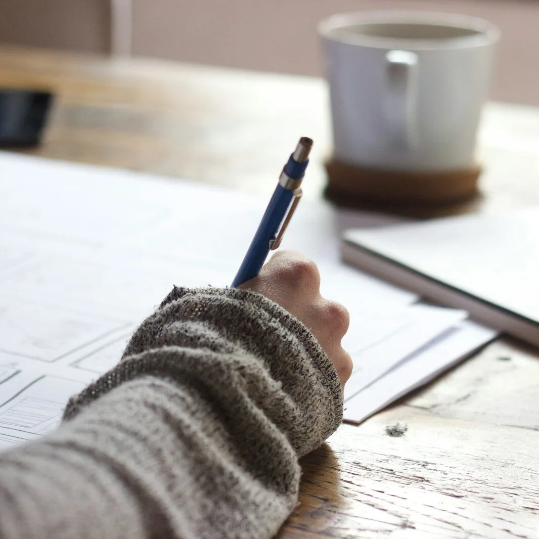 Home person writing on brown wooden table near white ceramic mug